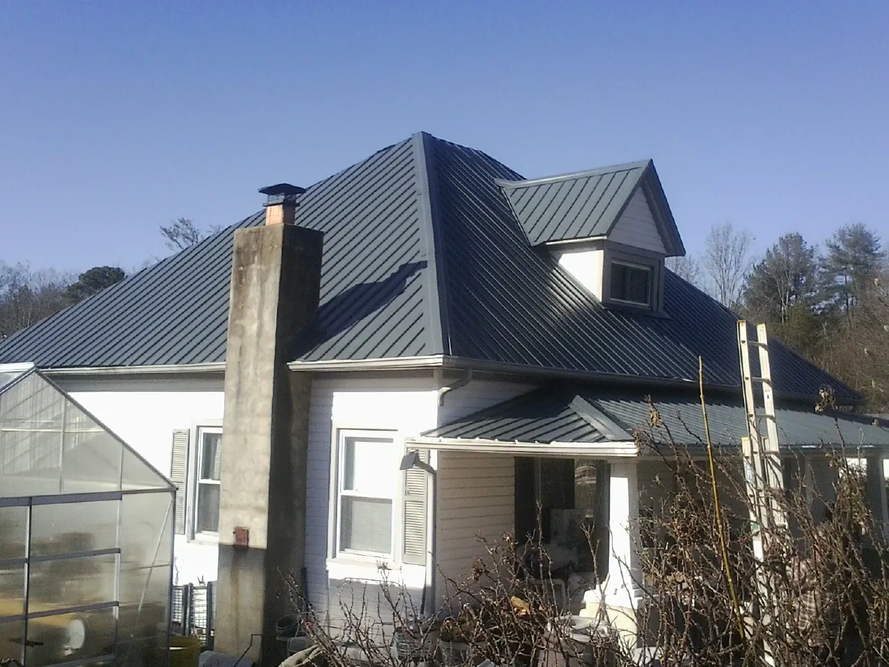 Dark blue standing seam metal roof on a white farmhouse with dormer — Slate & Tile Roof Repair by Roofing Brothers in Lemon Springs