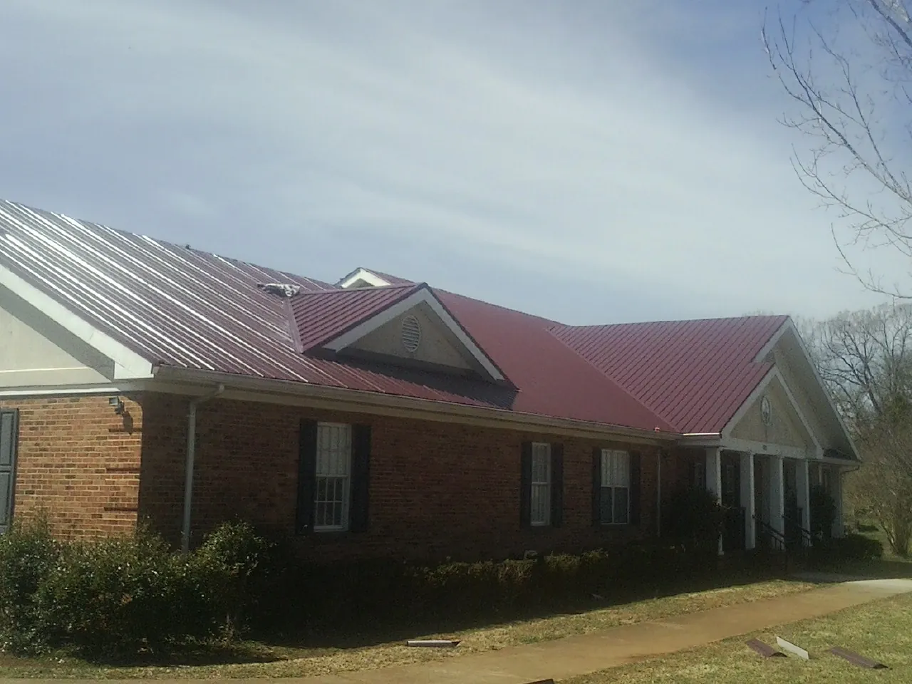 Red metal roof with gabled entries on a long brick building, from a Hail Damage Roof Repair job in Lemon Springs