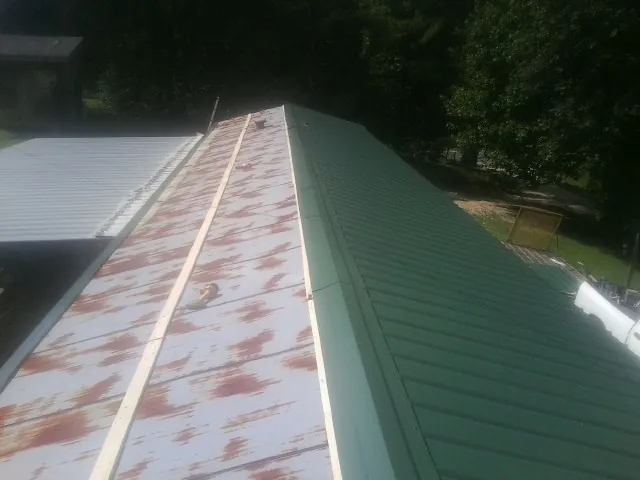 Old rusted panels beside newly installed green metal roofing — Wind Damage Roof Repair by Roofing Brothers in Lemon Springs