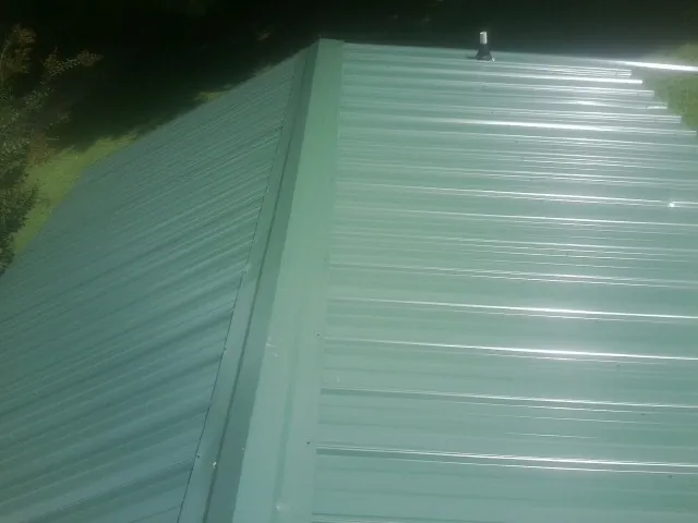 New green metal panels meeting at the ridge of a roof — Flat Roof Repair work by our crew in Lemon Springs