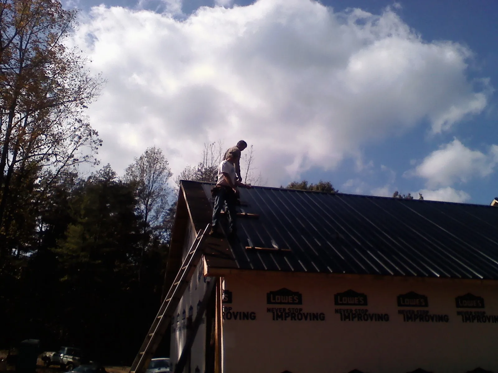Roofer fastening dark metal panels high against a cloudy sky, from a Roof Inspection job in Lemon Springs