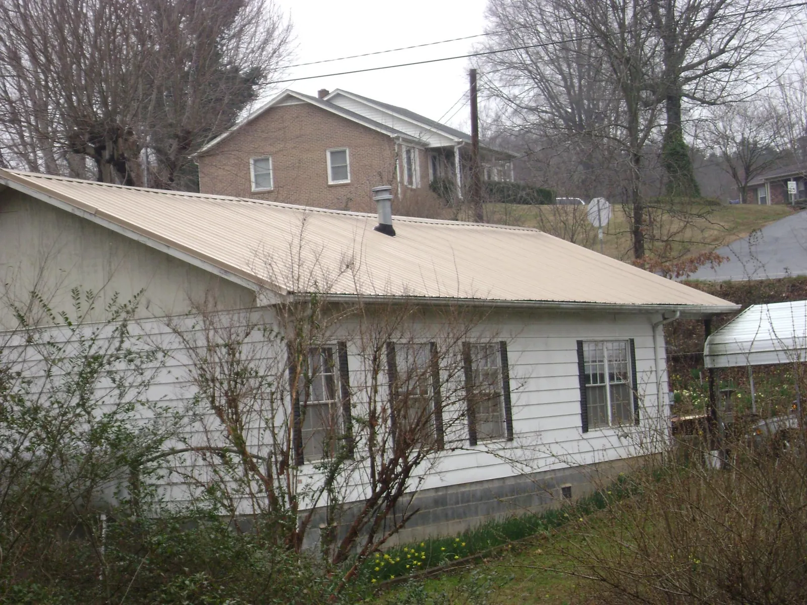 Tan metal roof on a white sided house set into a hillside — Commercial Roofing by Roofing Brothers in Lemon Springs